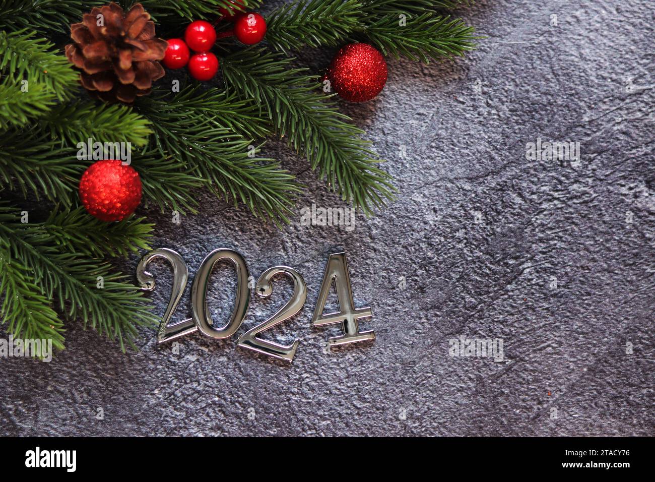Happy New Year 2024, Tannenzweig und Weihnachtskugeln auf grauem Hintergrund. Neujahrskarte, leerer Platz. Weihnachtszweig, silberne Zahlen 2024. Selektiv Stockfoto