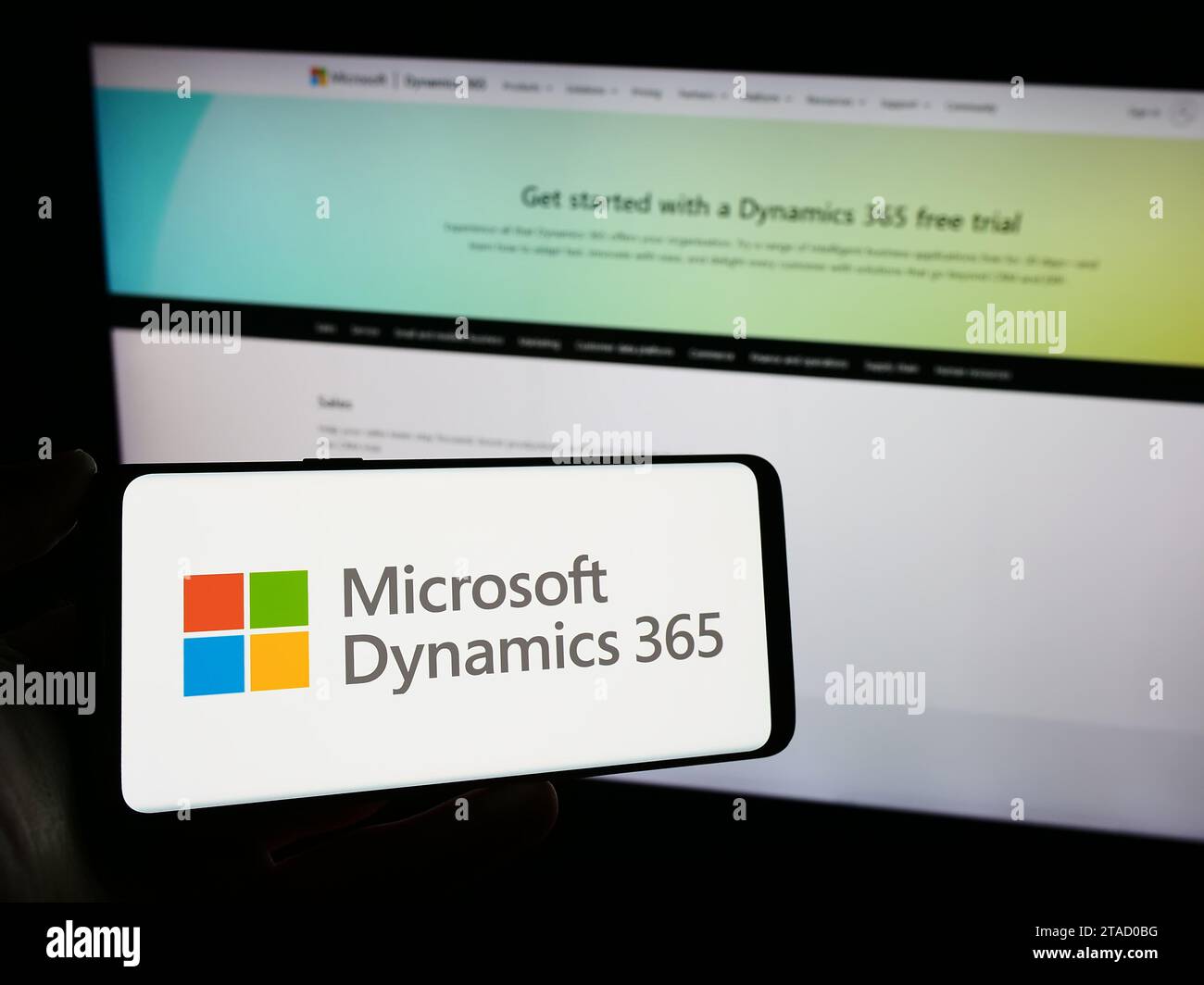 Person, die ein Mobiltelefon mit dem Logo des Buchhaltungssoftwareprodukts Microsoft Dynamics 365 vor der Unternehmenswebseite hält. Schwerpunkt auf dem Display des Telefons. Stockfoto