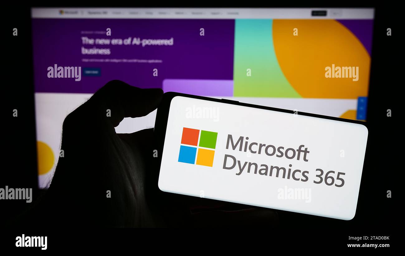 Person, die ein Mobiltelefon mit dem Logo des Buchhaltungssoftwareprodukts Microsoft Dynamics 365 vor der Unternehmenswebseite hält. Schwerpunkt auf dem Display des Telefons. Stockfoto