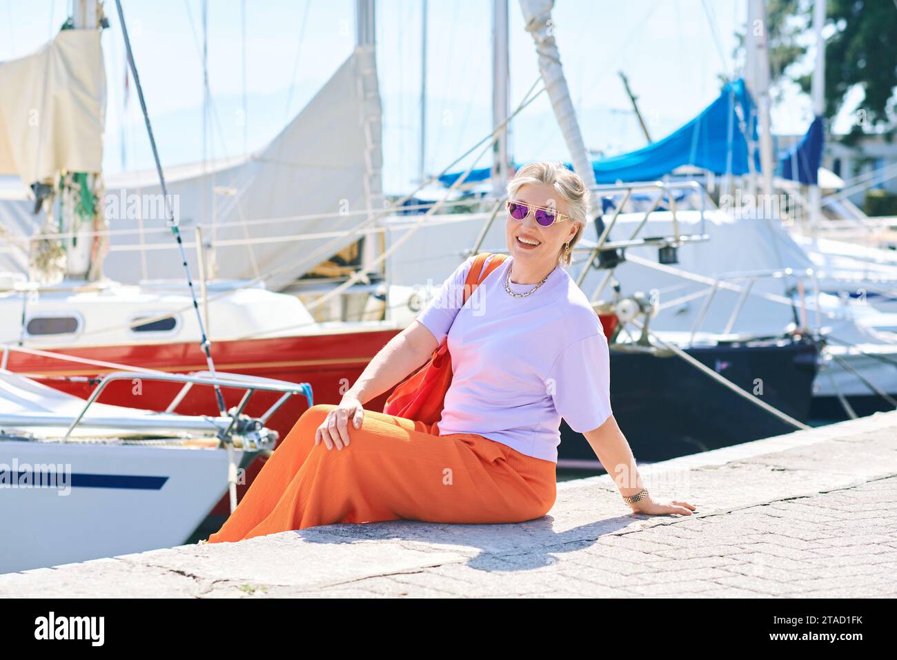 Outdoormodeporträt von mittlerem Alter 50 - 55 Jahre alte Frau in bunten Outfit, posiert am See oder Hafen, Reise- und Urlaubsleben Stockfoto