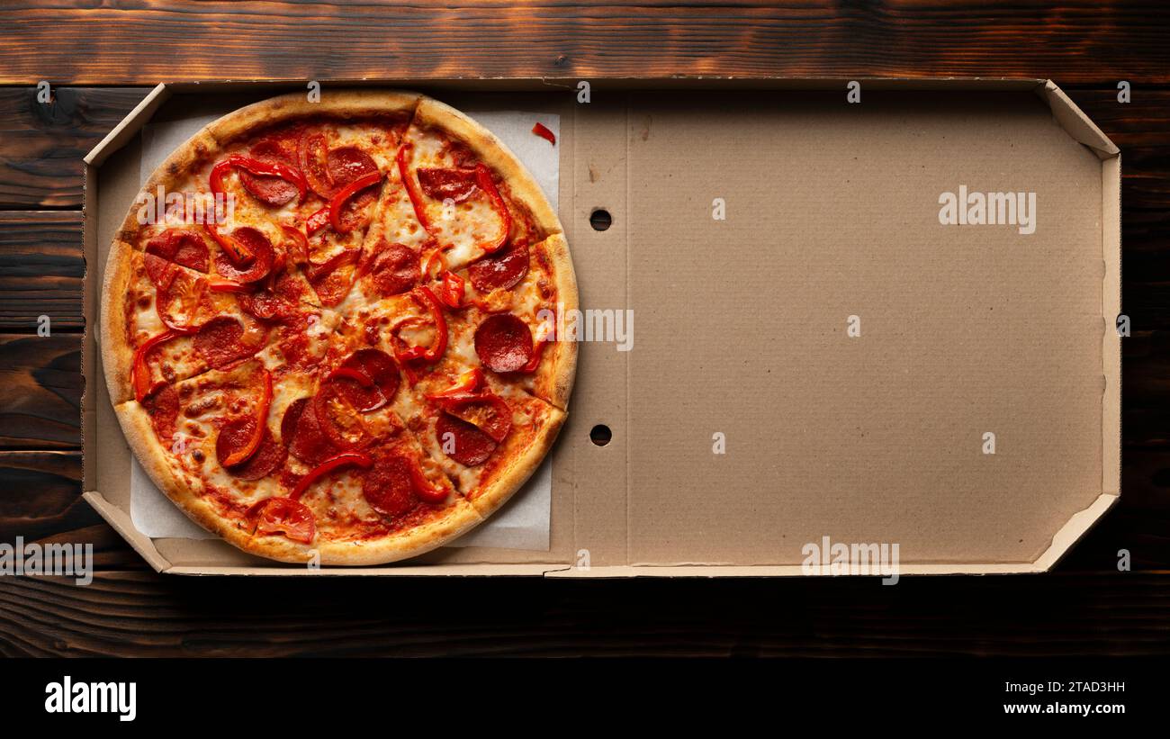 Paprika-Pizza mit Paprika in offener Kartonbox auf dunklem Holztisch flach liegend mit Kopierraum Stockfoto
