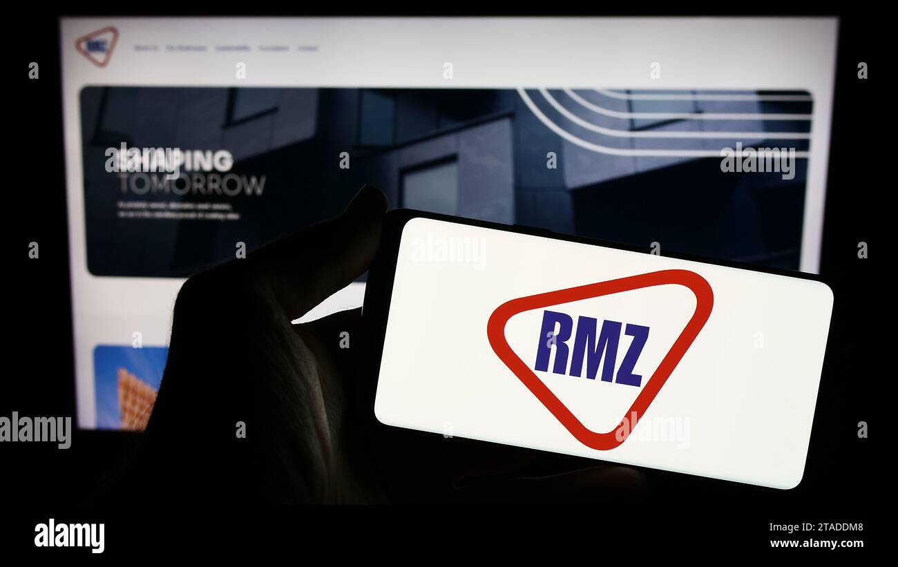 Person, die ein Smartphone mit dem Logo der indischen Immobiliengesellschaft RMZ Corp. Vor der Website hält. Schwerpunkt auf dem Display des Telefons. Stockfoto