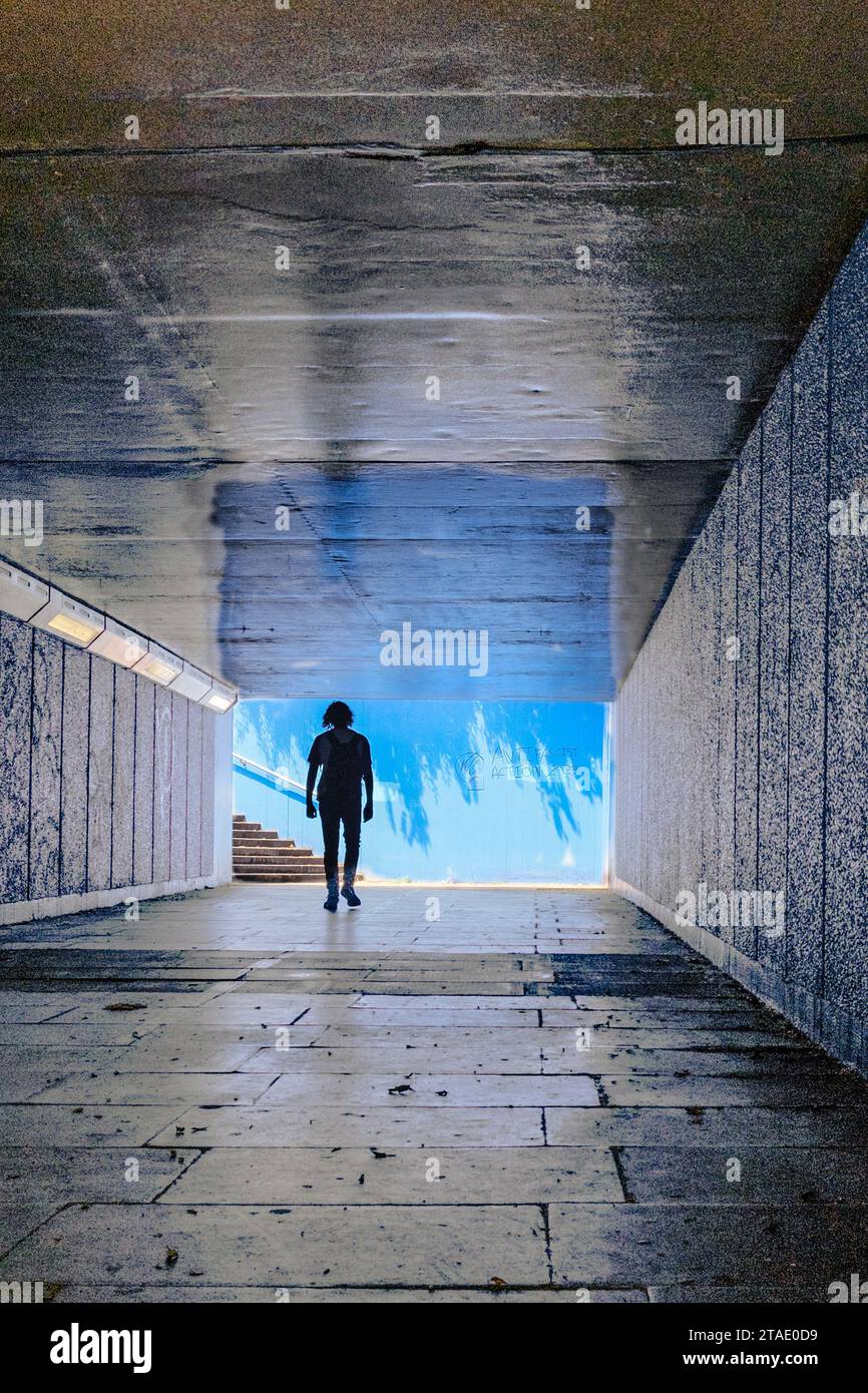 Silhouette eines Einzelgängers, der durch eine unterirdische Londoner Passage mit führenden Linien, Schatten und Reflexionen geht. Stockfoto