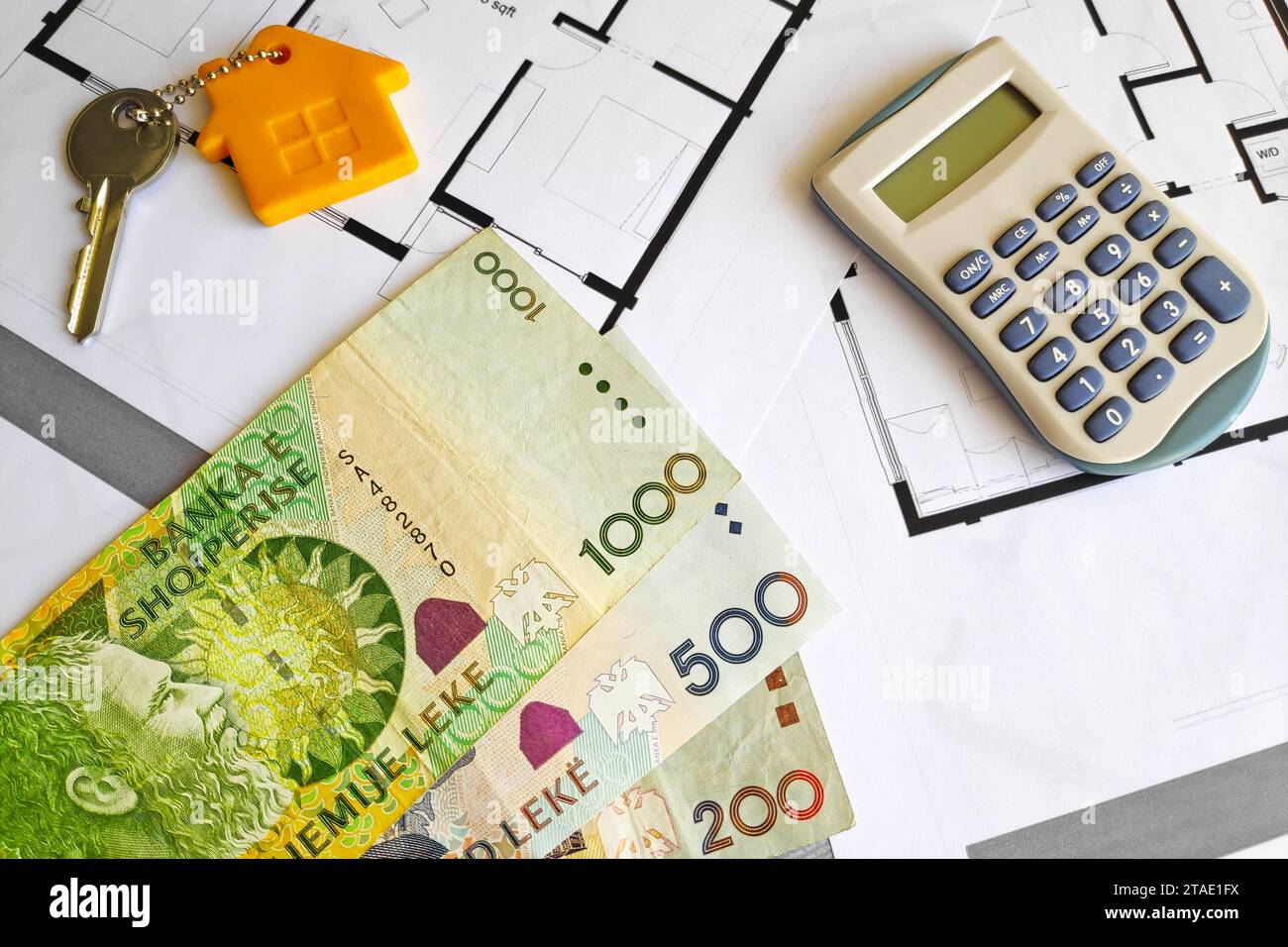Nahaufnahme einiger albanischer Lek-Banknoten, eines Hausschlüssels und eines Taschenrechners oben auf den Bauplänen. Stockfoto