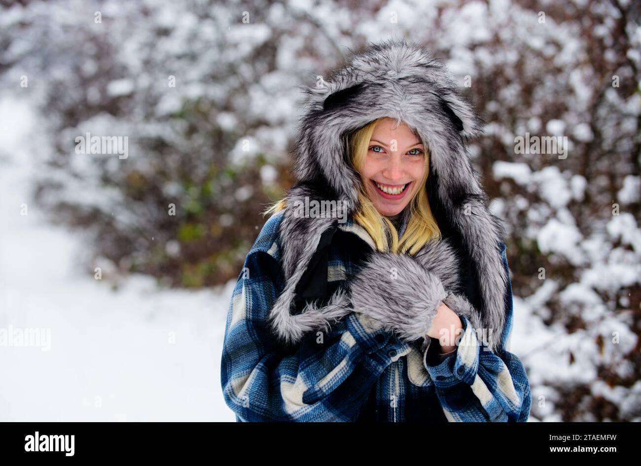 Wintermode. Schöne Frau in warmer Kleidung im Winterpark. Stilvolles weibliches Model, das in der Natur im Winter spaziert. Lächelndes Mädchen im karierten Mantel, Pelzmütze Stockfoto