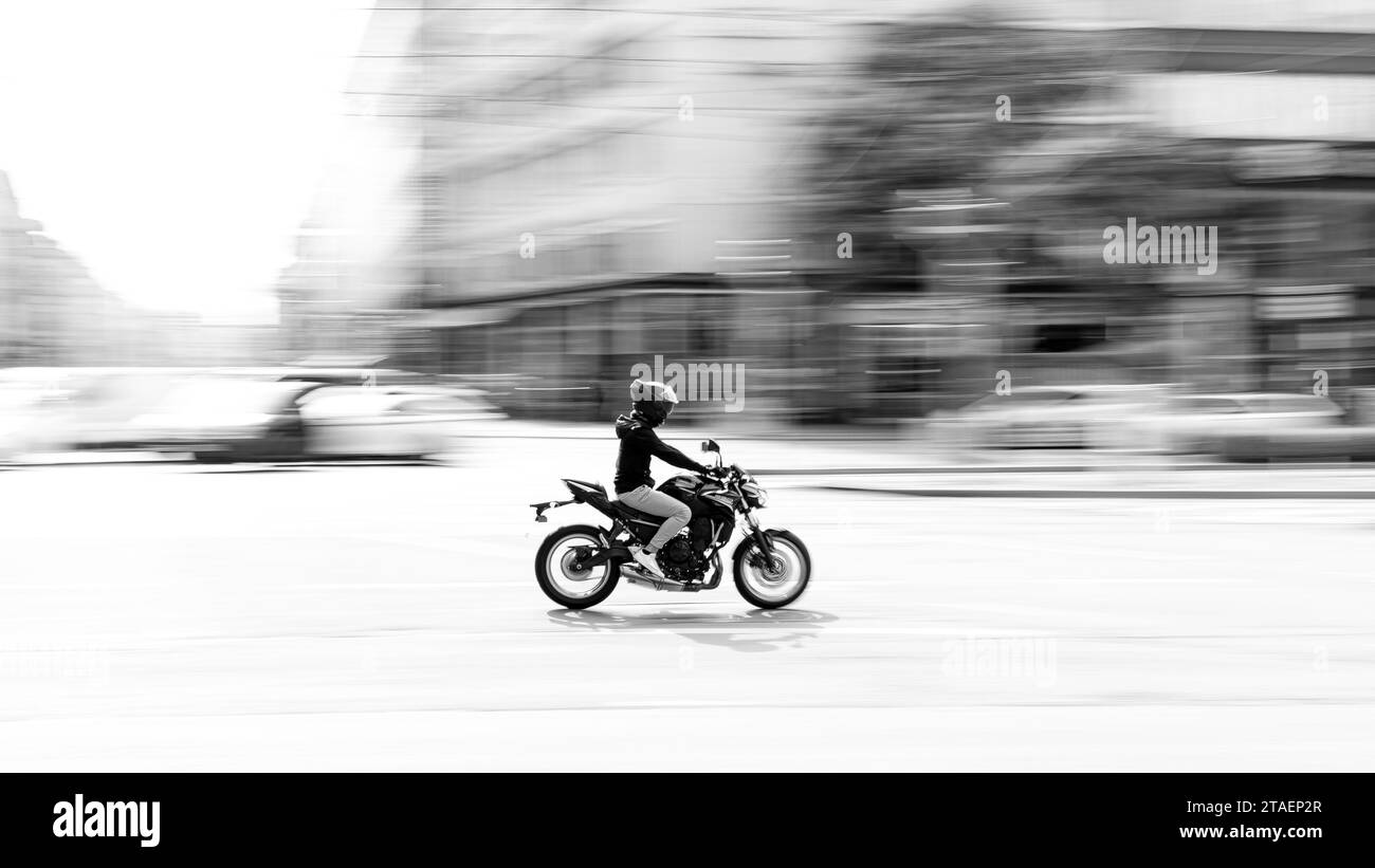 Ein erwachsener Mann, der einen Helm trägt und mit einem Motorrad fährt, fährt durch eine Kreuzung auf einer Stadtstraße Stockfoto