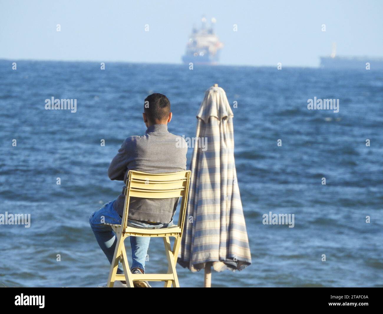 Ein junger Mann von hinten, der allein auf einem Stuhl am Ufer des Mittelmeers sitzt, unerkannte Person, die am Strand sitzt, Depression, ich Stockfoto