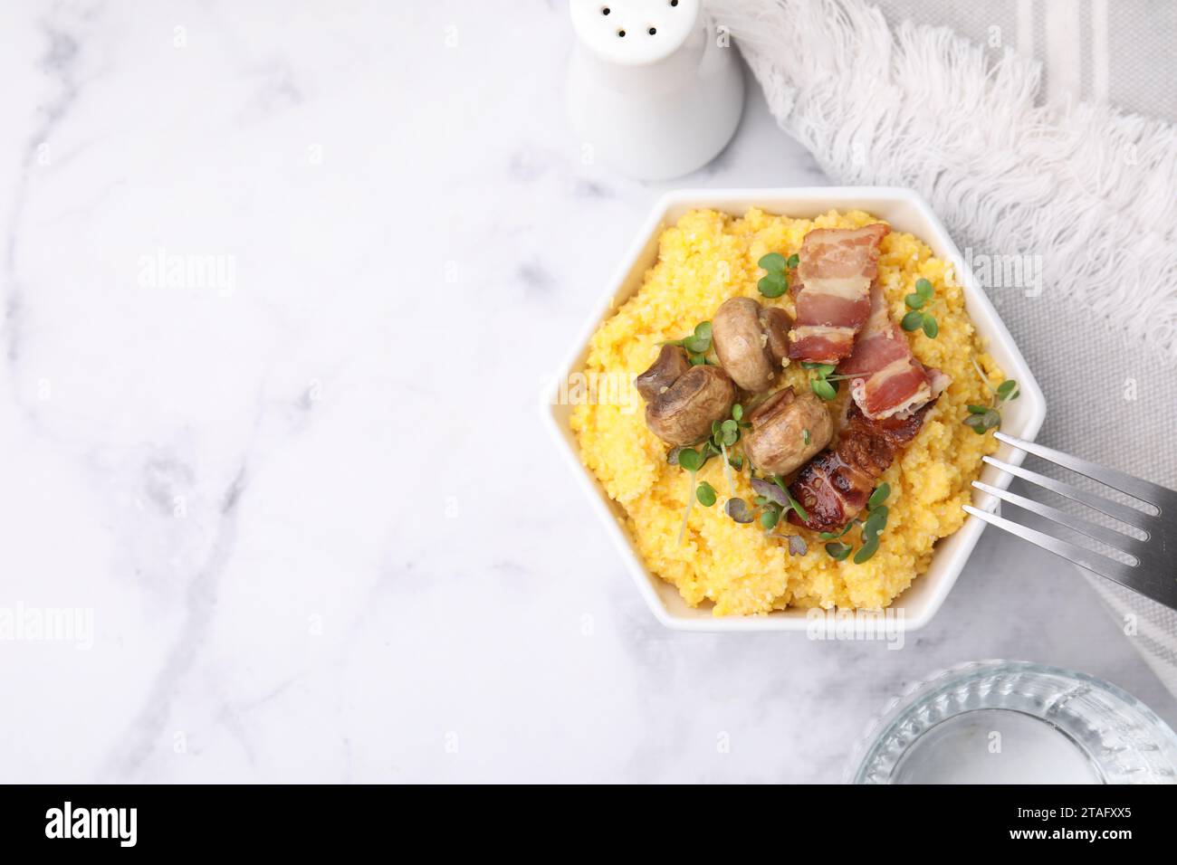 Gekochtes Maismehl mit Speck, Pilzen und Mikrogrün in Schüssel auf weißem Marmortisch, Blick von oben. Leerzeichen für Text Stockfoto