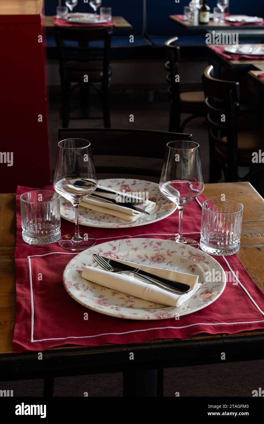 Ein kleiner Holztisch für zwei Gäste ist elegant mit Tellern, Gläsern, Besteck, Gabel und Messer sowie Servietten in einem kleinen Café in Florenz, Italien, eingerichtet. Stockfoto