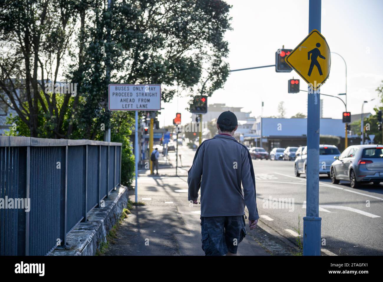 Mann, der auf dem Fußgängerweg der Stadtstraße läuft. Straßenschilder und Ampeln an der Kreuzung. Auckland. Stockfoto