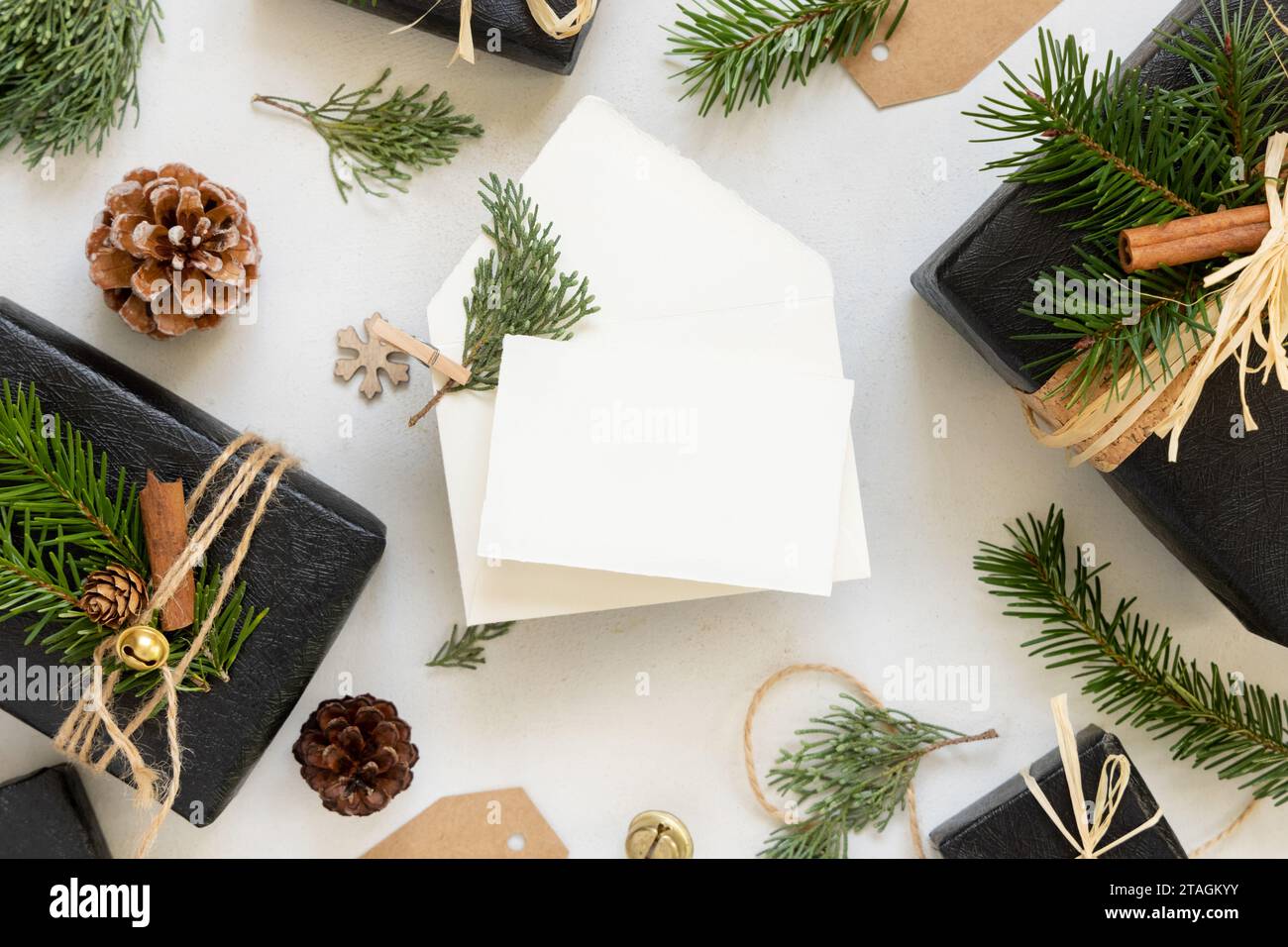 Pappkarte zwischen Weihnachtsdekor, schwarzen Geschenkboxen und grünen Tannenzweigen von oben. Horizontales leeres Kartenmodell, flache Ladefläche, Kopierraum. Weihnachten oder Stockfoto