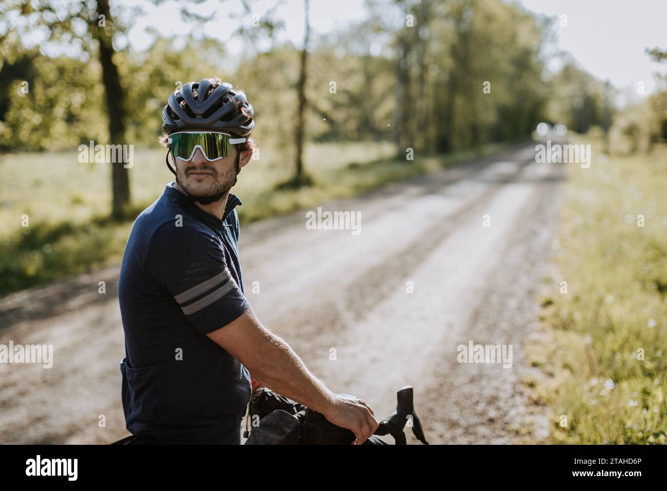Radfahrer mit Helm und Sonnenbrille schaut die Schotterstraße hinunter Stockfoto