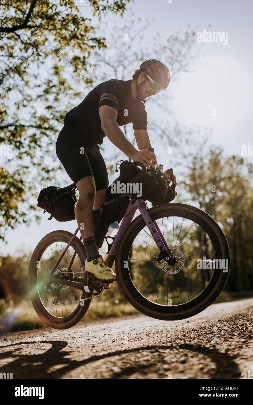 Männlicher Radfahrer auf einem lila Fahrrad macht einen Hasen auf Schotterpiste Stockfoto
