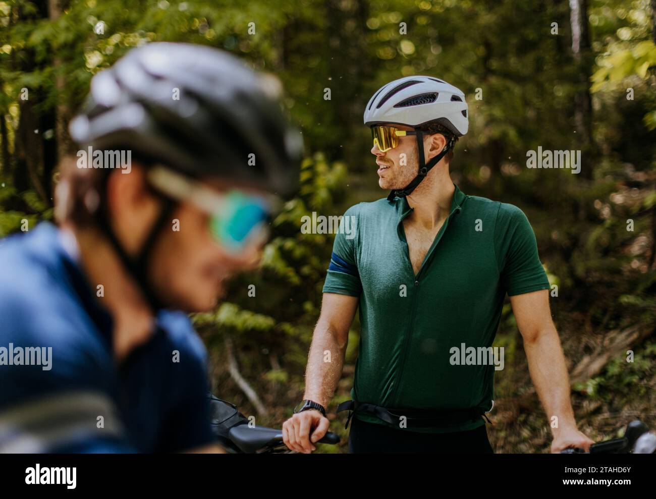 Zwei männliche Radfahrer mit Sonnenbrille und Fahrradhelmen in einem bewaldeten Gebiet Stockfoto