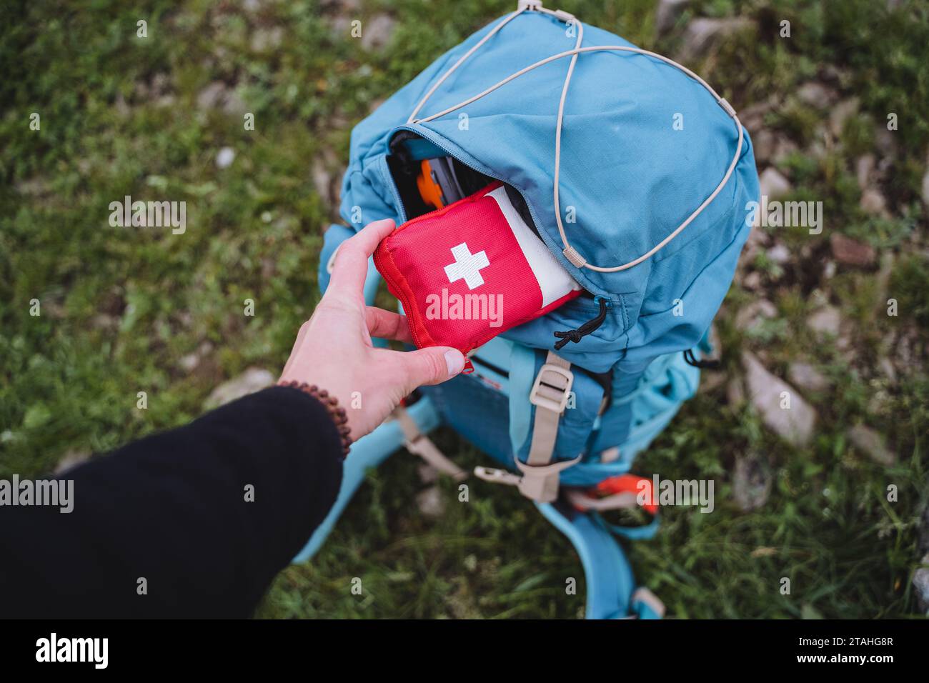 Ein erste-Hilfe-Kasten befindet sich in einem Rucksack, eine Hand hält einen Beutel mit Medikamenten. Stockfoto