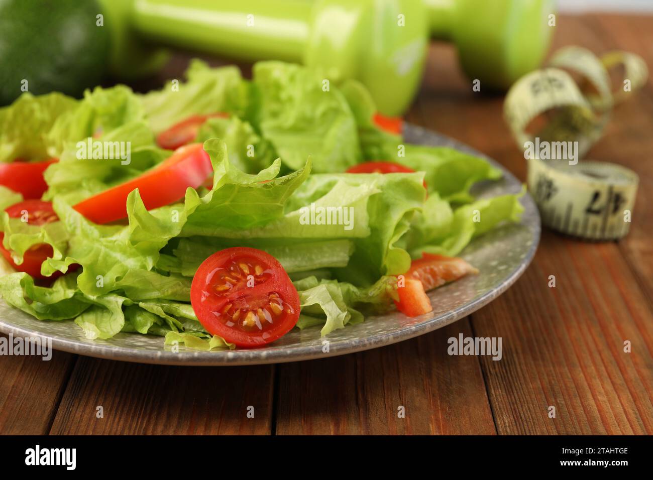 Gesunde Ernährung. Salat, Kurzhanteln und Maßband auf Holztisch, Nahaufnahme Stockfoto