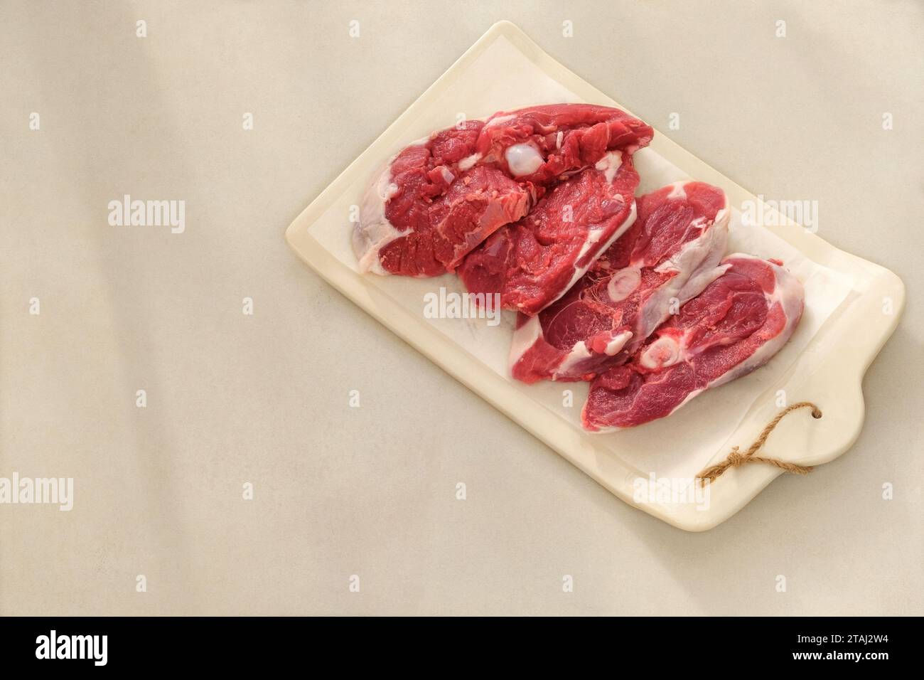 Lammfleisch auf einem Keramikbrett auf beigefarbenem Hintergrund. Fleisch zum Kochen. Hinterer Teil des Schlachtkörpers. Draufsicht. Stockfoto