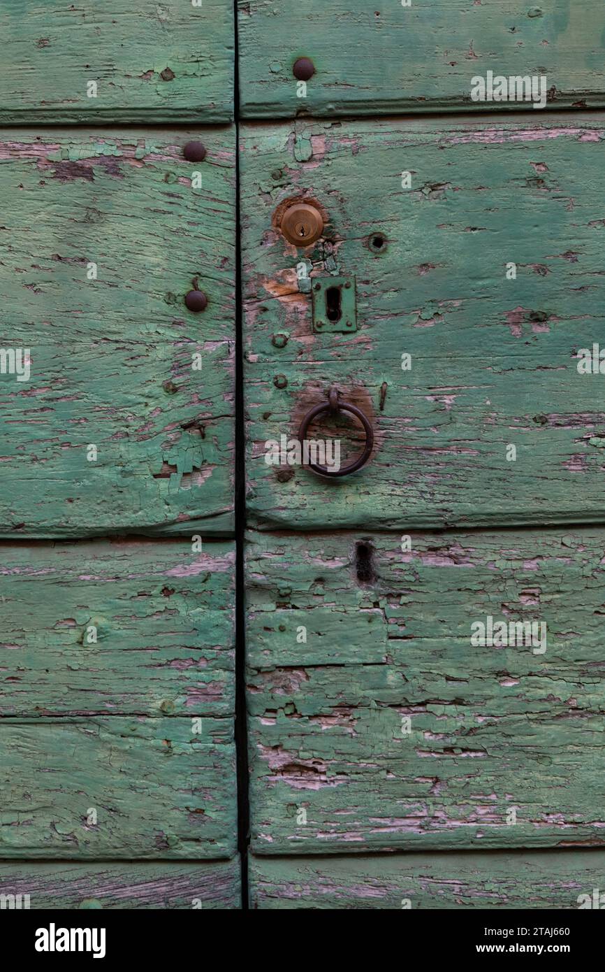 Eine verblasste, abblätternde und verwitterte, hellgrün lackierte Tür mit abgebrochener Oberfläche, Schlüssellöchern, Schloss und rostfreiem Metallklopfer. Stockfoto