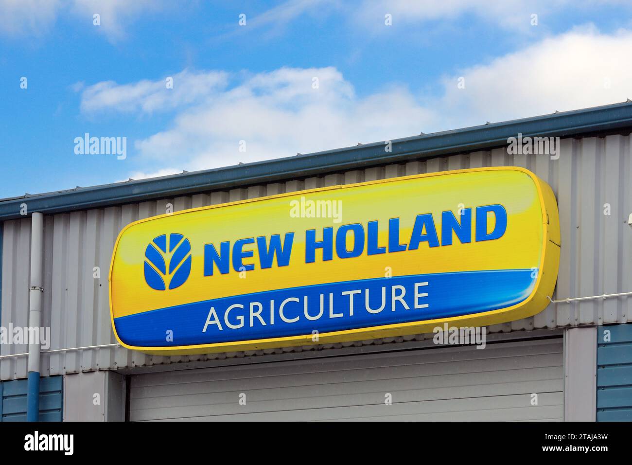 New Holland Agriculture Logo außen am Händlerbetrieb mit blauem Himmel und Wolken, etwas Schnee fällt. Salo, Finnland. November 2023. Stockfoto