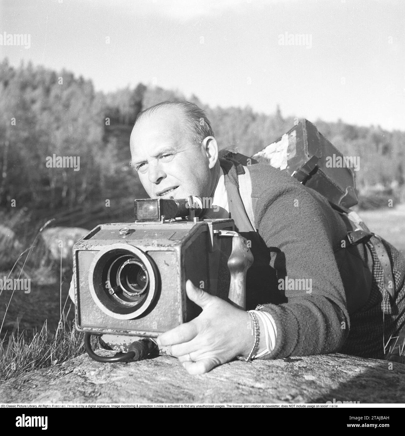 Kameramann in den 1940er Jahren Gustaf Boge, 1891–1975, schwedischer Kameramann. Vor allem bekannt für Dreharbeiten für die schwedische Filmindustrie und die Zeitschrift SF, die ein Kurzfilm war, in dem Nachrichten und Ereignisse in einer Art Dokumentarfilm dokumentiert wurden. Früher wurde es in Kinos gezeigt, meist vor einem Spielfilm. Hier ist Gustaf Boge auf einer Filmmission in Vålådalen zu sehen, wo er die Kamera im besten Scharfschützenstil hochhebt. 1942. Kristoffersson Ref. B63-3 Stockfoto