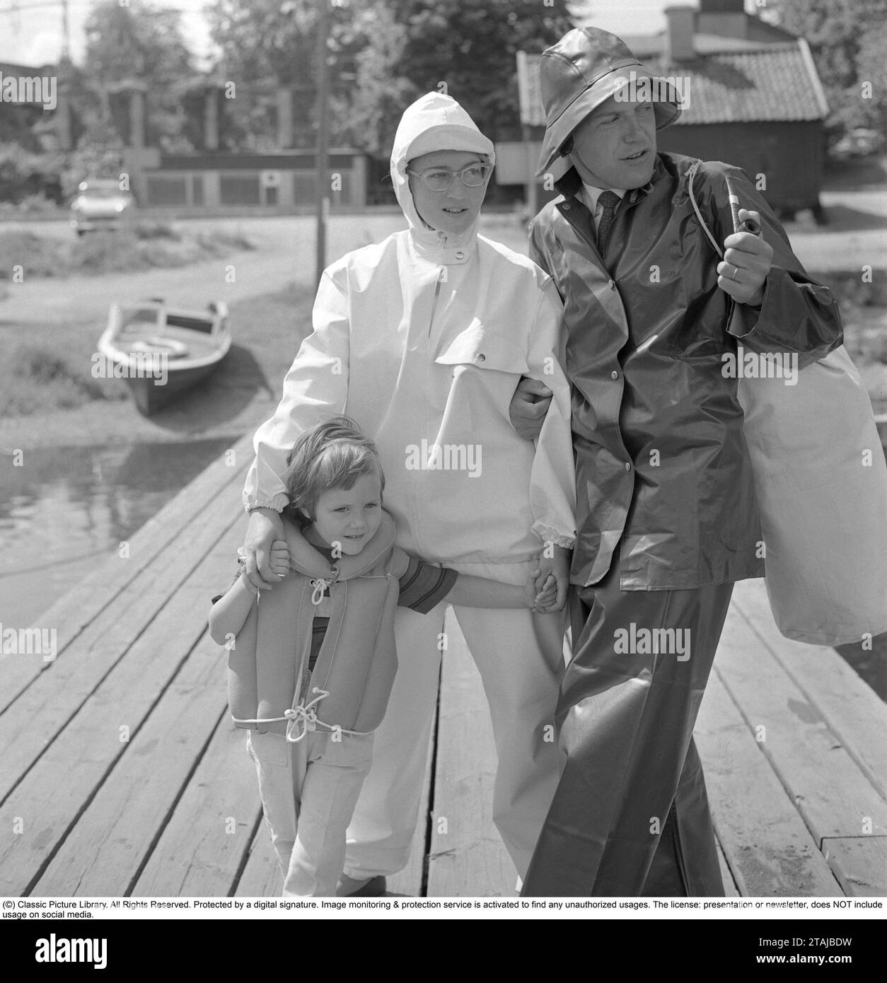 Regen in den 1950er Jahren Eine Familie, die für einen regnerischen Tag richtig gekleidet ist, in Regenmänteln und Hüten, die vor Nässe schützen. Schweden 1960. Stockfoto