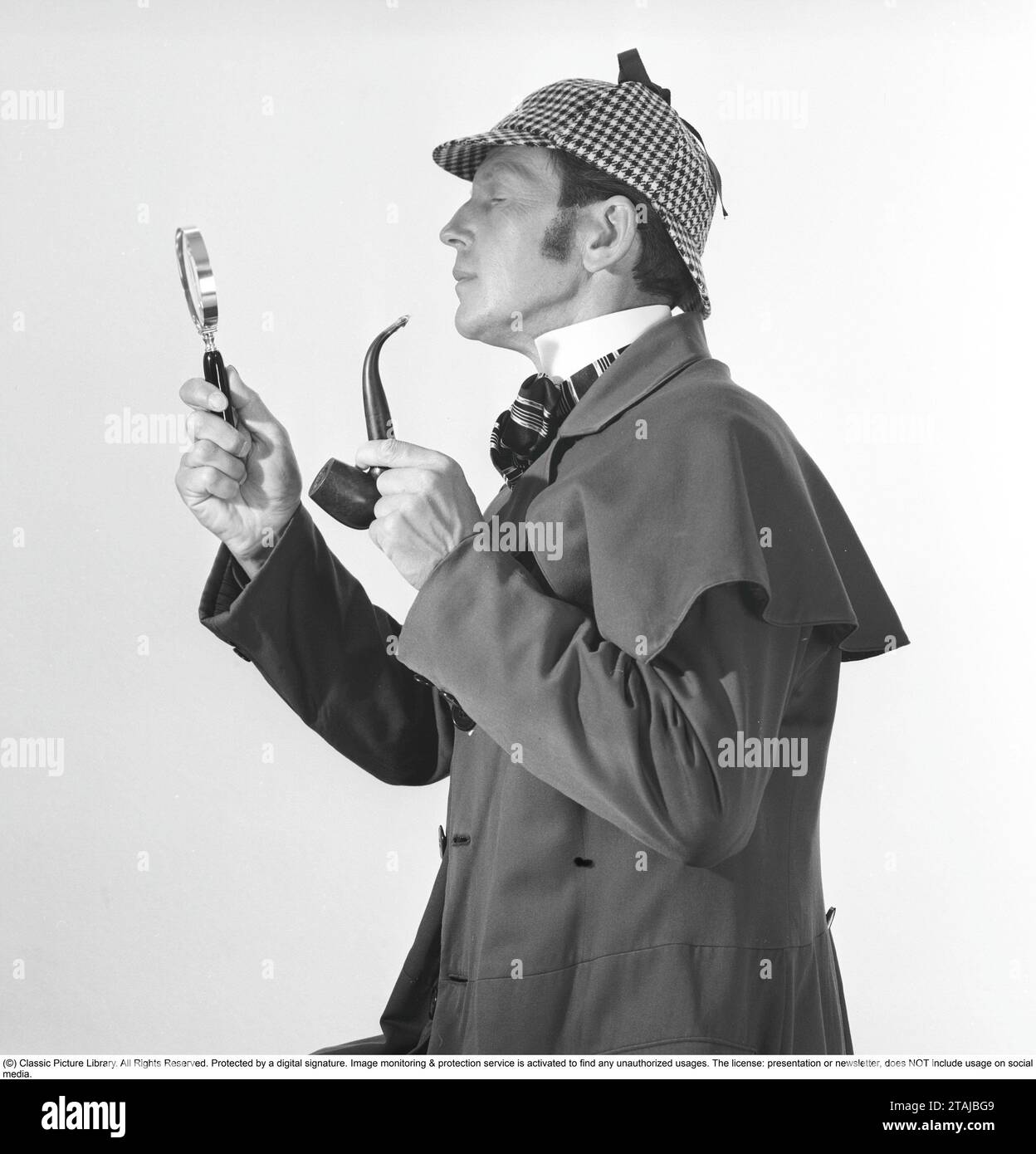 Detective spielen. Ein Mann in den typischen Kleidern des berühmten fiktiven Detektivs Sherlock Holmes sieht durch eine Lupe aus. Stockfoto