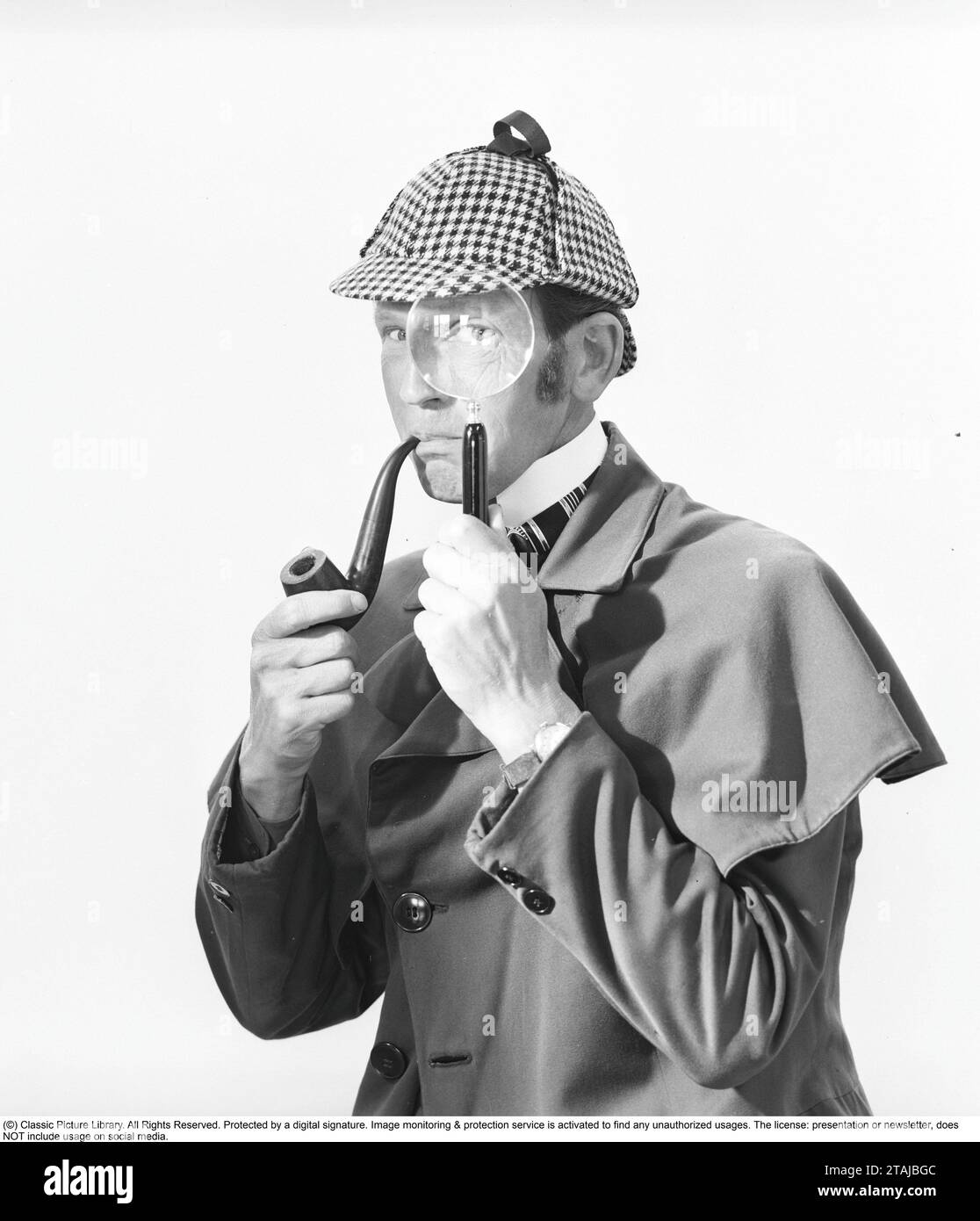 Detective spielen. Ein Mann in den typischen Kleidern des berühmten fiktiven Detektivs Sherlock Holmes schaut durch eine Lupe in die Kamera. Stockfoto