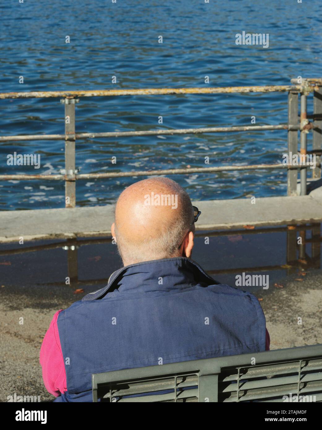 Ein älterer Mann sitzt auf einer Bank am Wasser Stockfoto