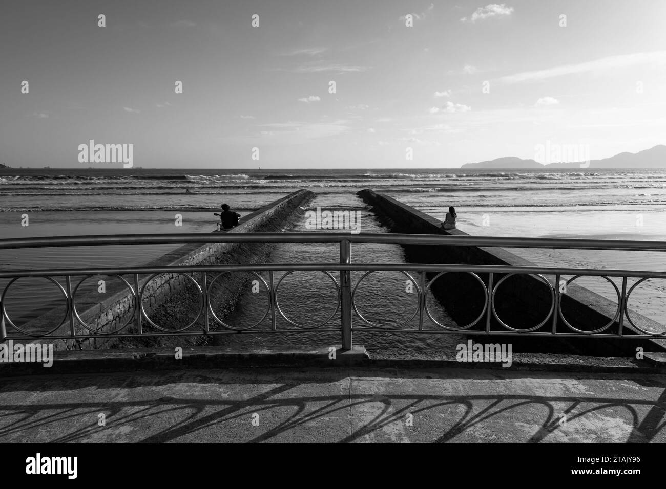 Stadt Santos, Brasilien. Water Channel Bridge Nr. 6. Die Leute genießen den Strand an der Wand. Bucht und Horizont im Hintergrund. Schwarzweißbild Stockfoto