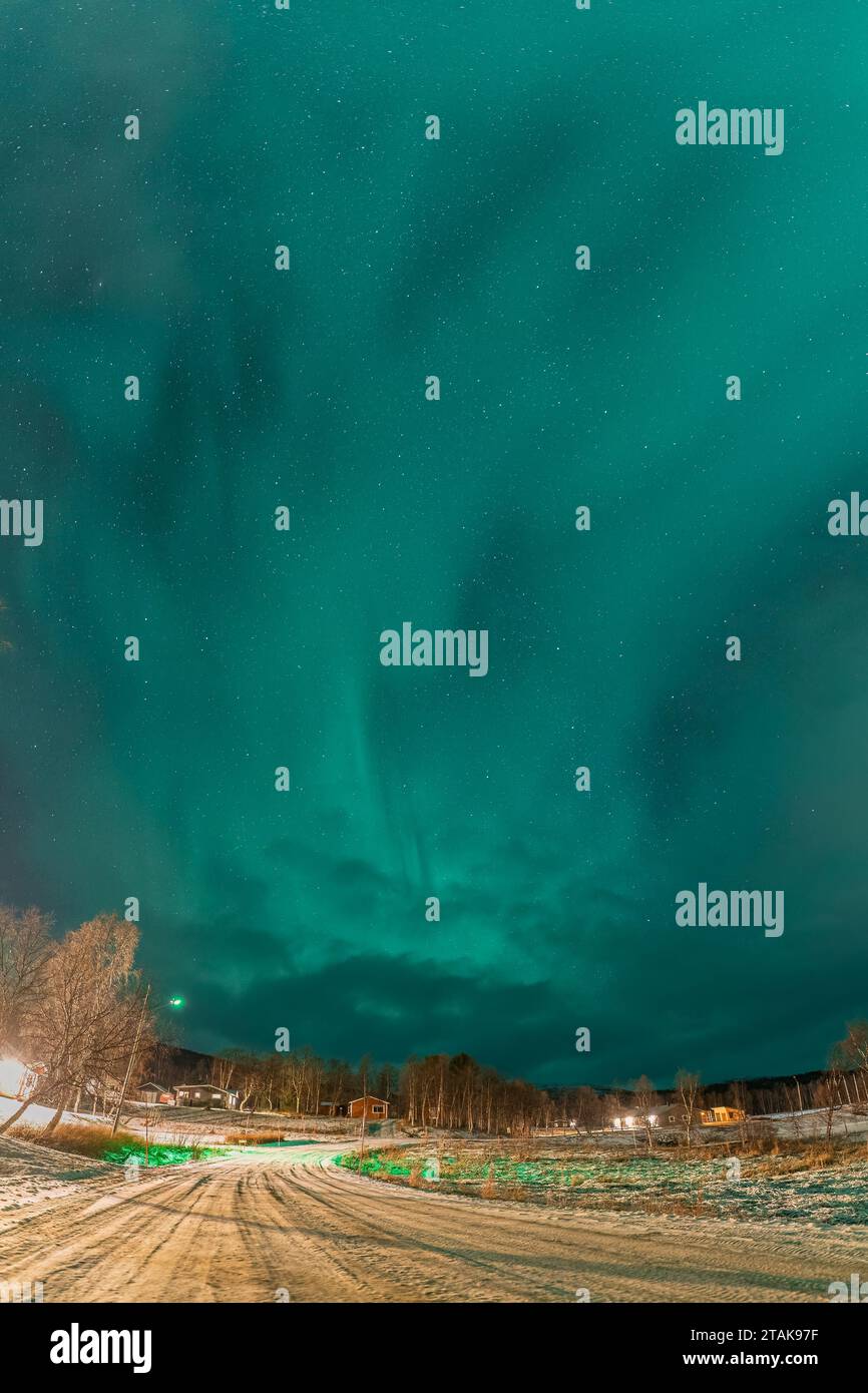 Vertikales Nachtfoto von Nordlichtern über einer Straße in einem kleinen Bergdorf in Nordschweden, Lappland, Joesjo. Grünes Licht von Aurora Borealis, wi Stockfoto