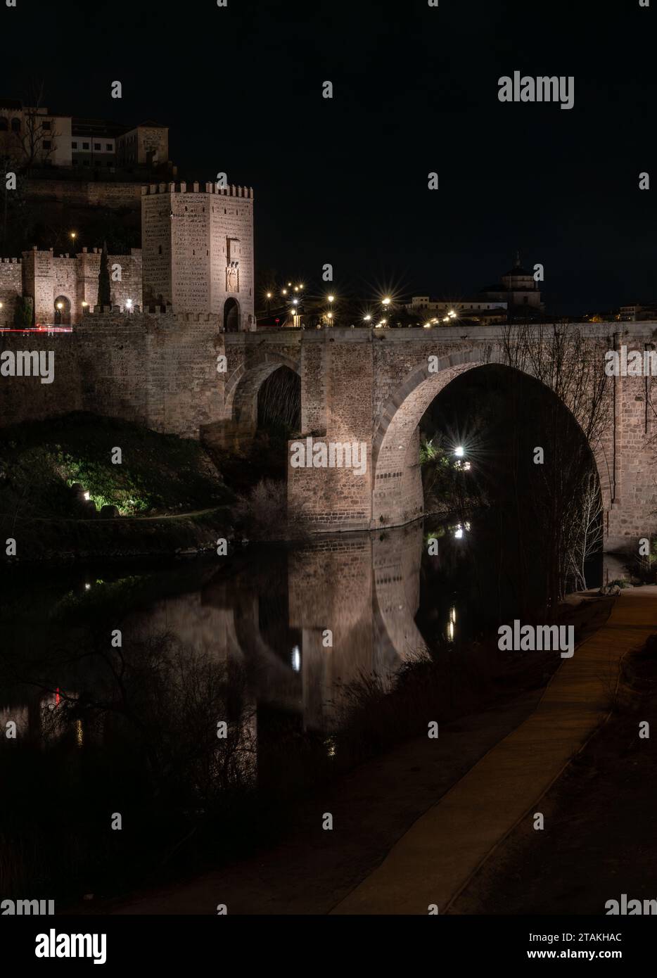 Alcantara-Brücke mit dem Turm am Eingang der Stadt und seiner Reflexion im Fluss Tejo mitten in der Nacht. Historisches Bauwerk Stockfoto