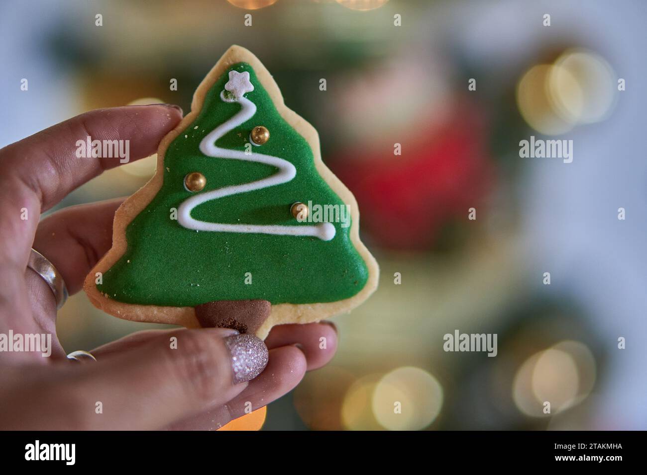 Frauenfinger halten einen süßen Keks in Form eines grünen Weihnachtsfestes. Kopierbereich und selektiver Fokus Stockfoto
