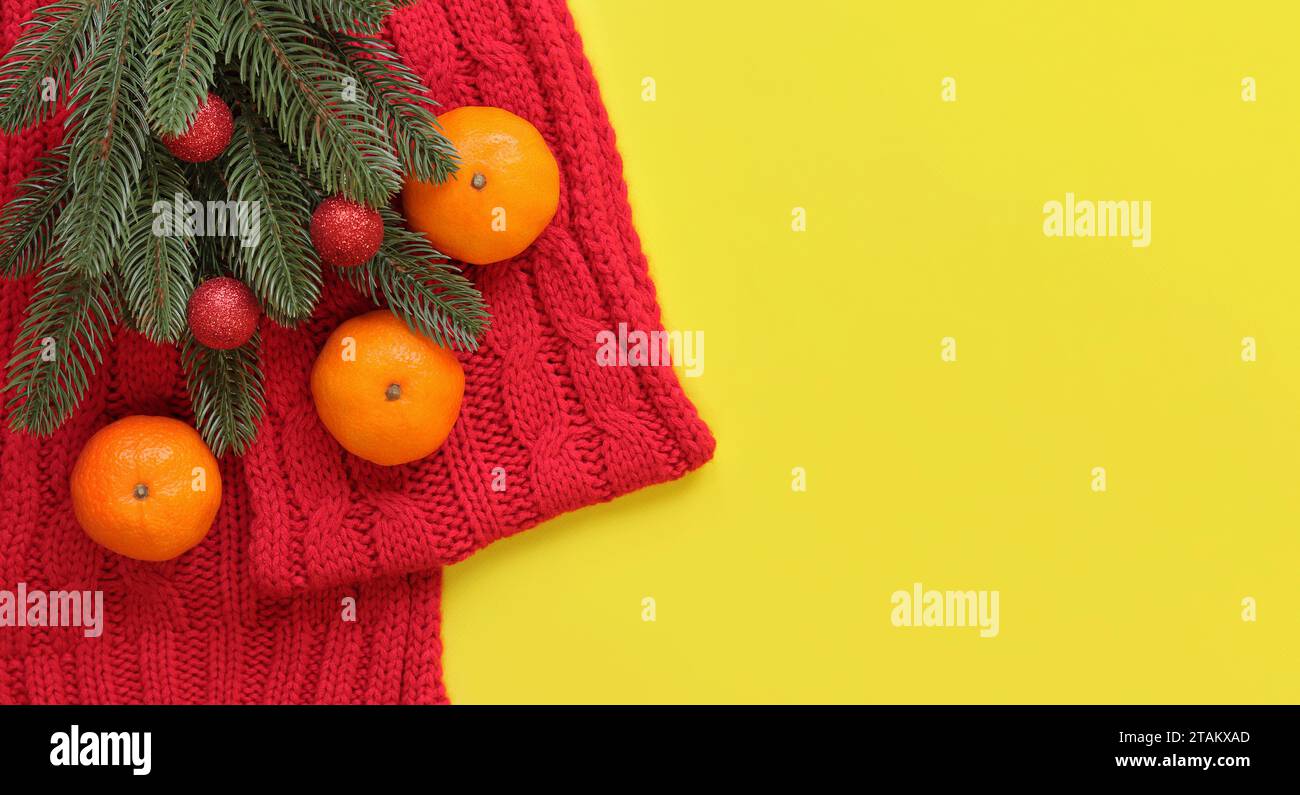 Roter Strickschal, Mandarinen und Fichtenzweig auf gelbem Hintergrund, Draufsicht, Kopierraum. Weihnachtskomposition, Neujahr, Banner. Neujahrskleie Stockfoto