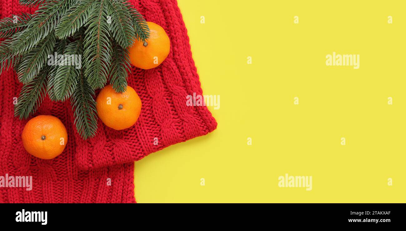 Roter Strickschal, Mandarinen und Fichtenzweig auf gelbem Hintergrund, Draufsicht, Kopierraum. Weihnachtskomposition, Neujahr, Banner Stockfoto