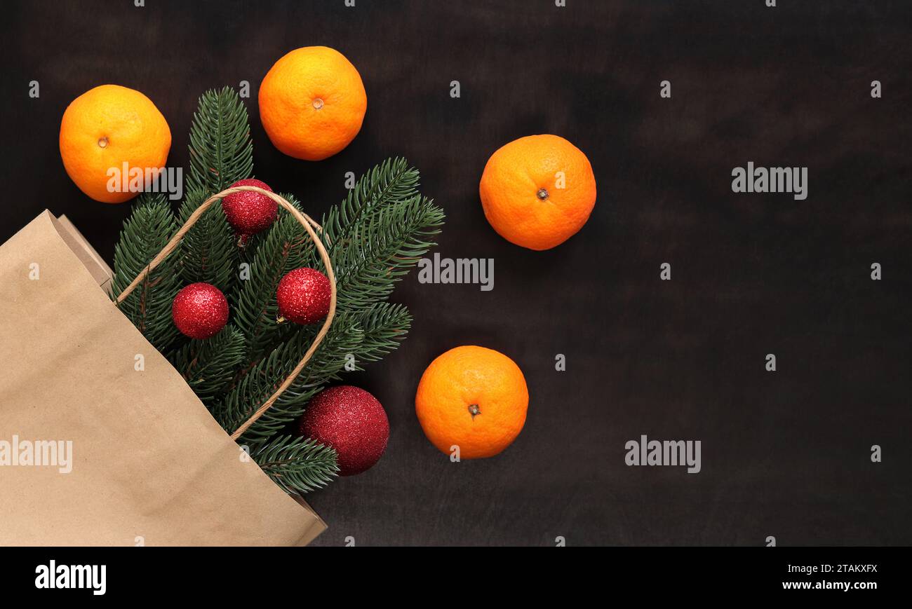Ein Fichtenzweig in einem Bastelbeutel, reife Mandarinen, ein Blick von oben auf die Gegenstände auf dem Tisch. Weihnachtskomposition, Neujahr. Kaufen Sie einen kleinen Weihnachtsbaum oder Stockfoto