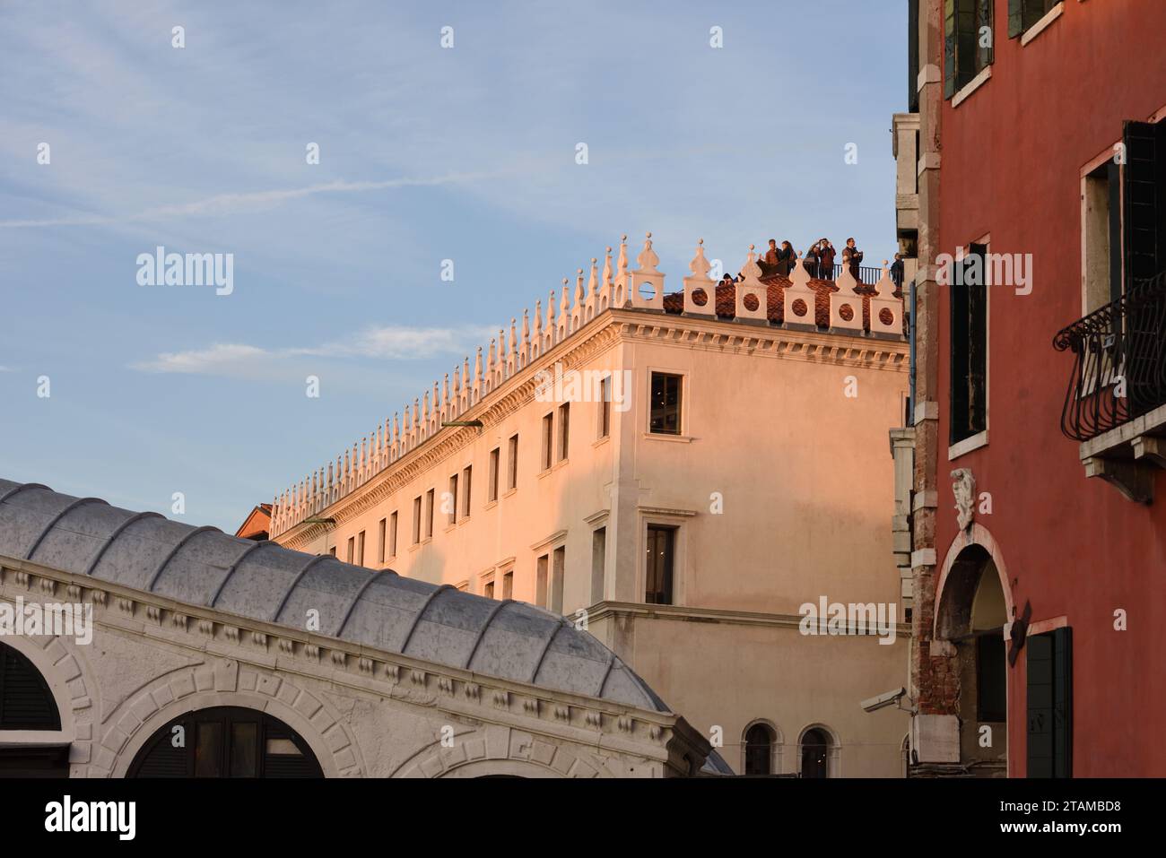 Touristen blicken über die Rialto-Brücke und den Canal Grande und genießen die Skyline von Venedig vom Dach des Fondaco dei Tedeschi, wenn sich der Sonnenuntergang nähert. Stockfoto