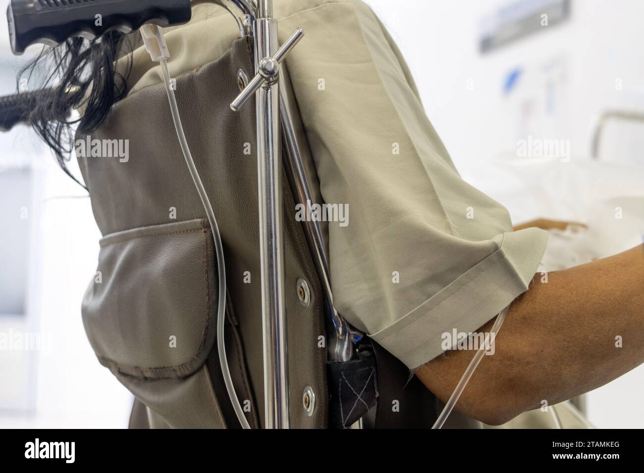 Ein Patient mit einer Infusion sitzt in einem Rollstuhl und wartet darauf, von einem Arzt untersucht zu werden Stockfoto