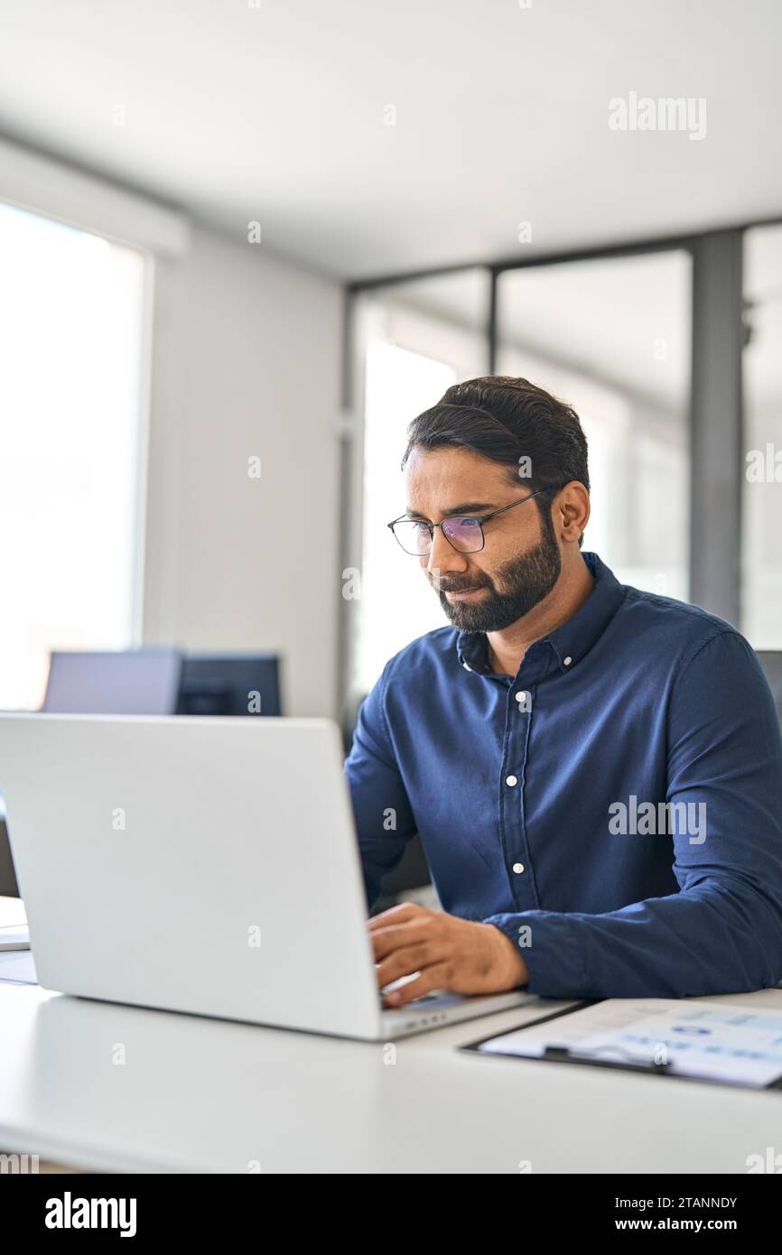 Beschäftigter, professioneller indischer Geschäftsmann, der im Büro mit einem Laptop arbeitet. Stockfoto