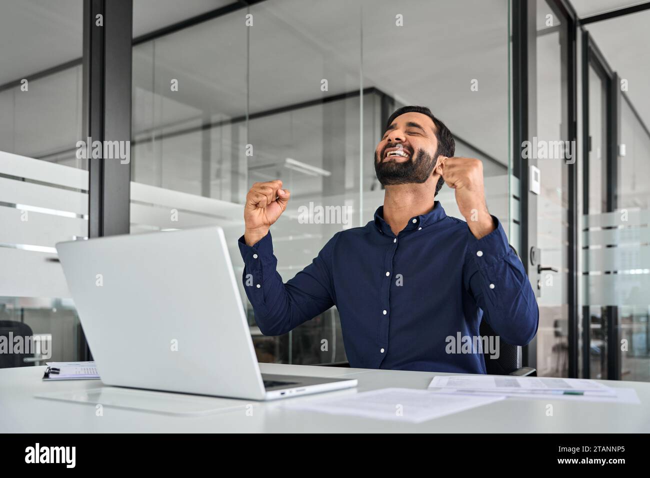 Glücklicher, aufgeregter, professioneller indischer Geschäftsmann, der mit einem Laptop den Sieg feiert. Stockfoto