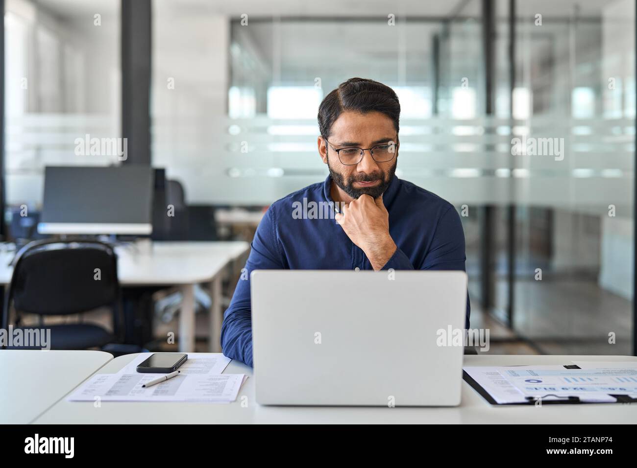 Beschäftigter indischer Geschäftsmann denkt über Datenmanagement und Arbeit an Notebooks nach. Stockfoto