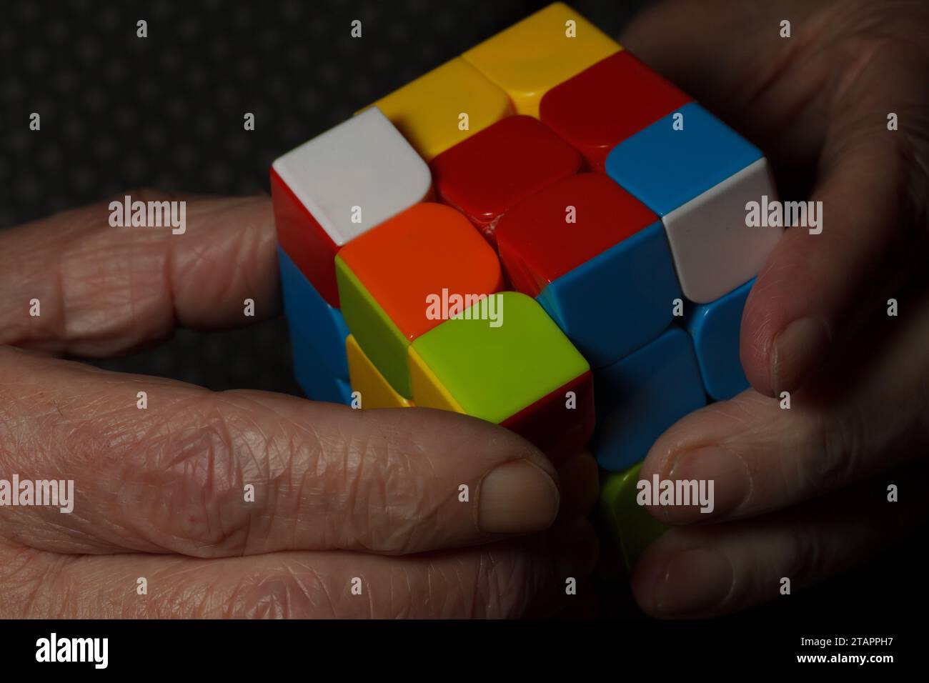 Die Hände des Seniors üben die Fingerbeweglichkeit mit einem rubikwürfel aus Stockfoto
