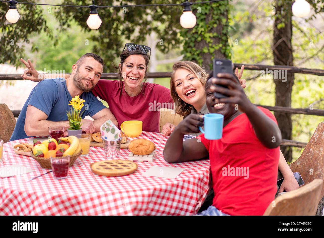 Eine vielfältige Gruppe von Freunden lacht und nimmt Selfies während eines Brunchs im Freien. Stockfoto