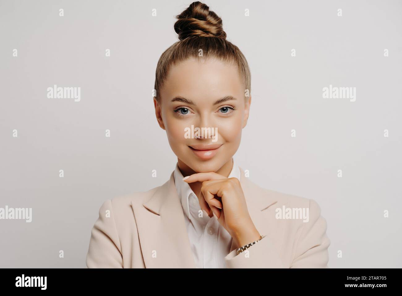 Selbstbewusste Geschäftsfrau in einem beigefarbenen Blazer mit einer durchdachten Handbewegung, die Professionalität widerspiegelt Stockfoto