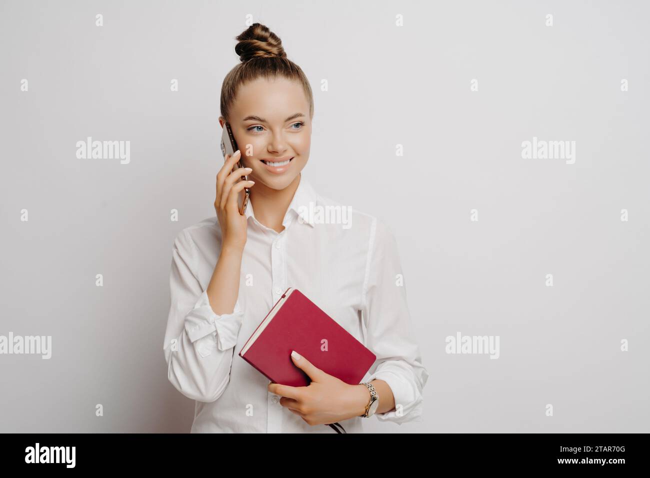 Lächelnde junge Frau, die mit einem Notebook in der Hand telefonierte, bedeutet Konnektivität Stockfoto