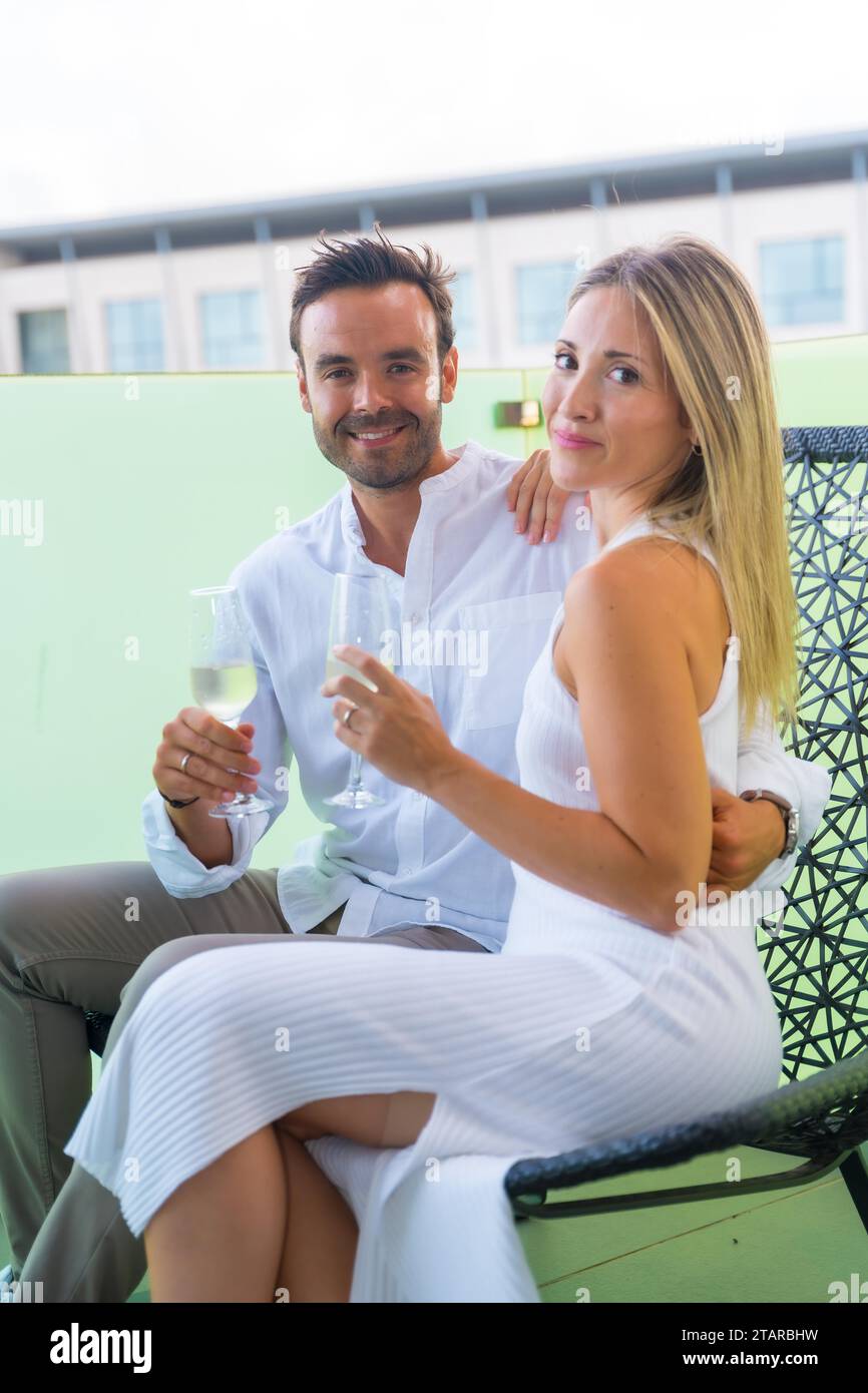 Vertikales Porträt von Liebhabern, die mit Champagner auf einem Stuhl auf der Terrasse eines Hotels ihre Liebe feiern Stockfoto