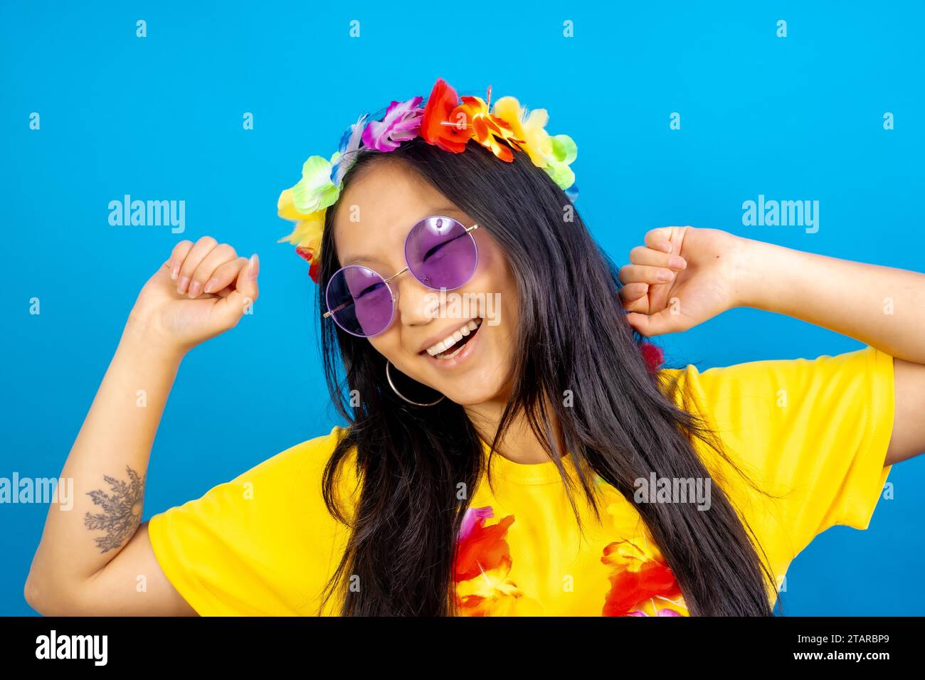 Studiofoto mit blauem Hintergrund einer Chinesin mit Sonnenbrille und hawaiianischer Blumenkrone Stockfoto