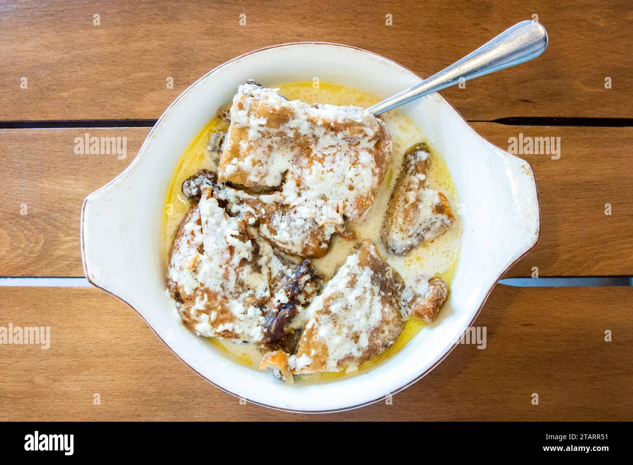 Reisen Sie nach Georgien - Blick von oben auf die Portion Chkmeruli (georgisches Gericht, Hühnchenstücke in cremiger Knoblauchsoße gebraten) in einer Schüssel auf einem Holztisch im lokalen Café Stockfoto