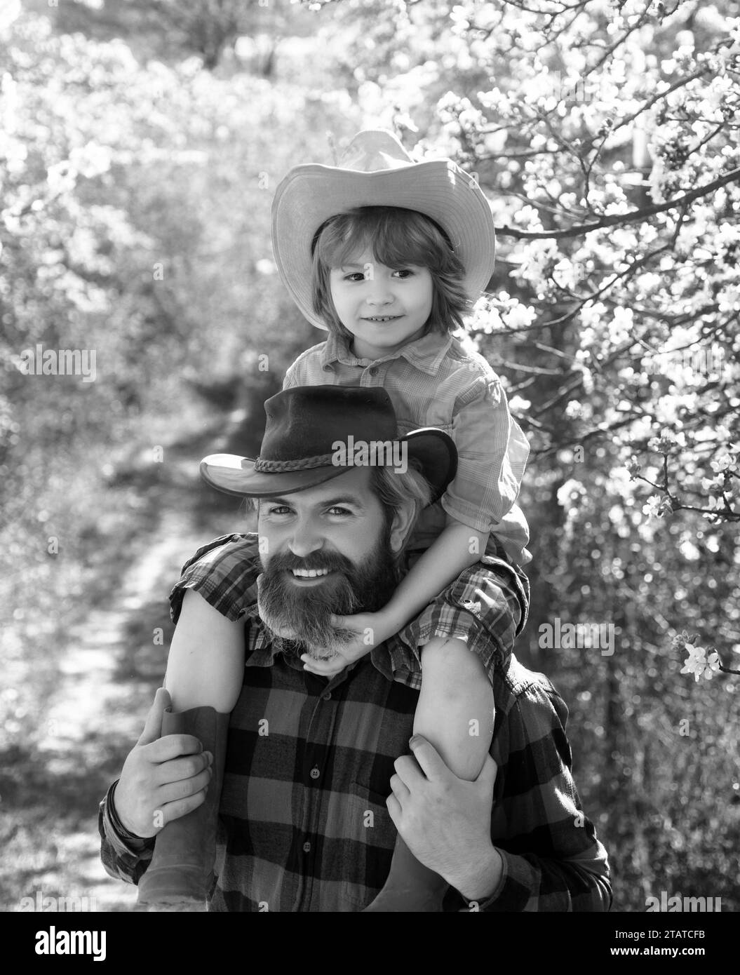 Sohn sitzt auf der Schulter des Vaters. Frühling Familie lächelnd Outdoor Park oder Garten an sonnigen Tag. Stockfoto