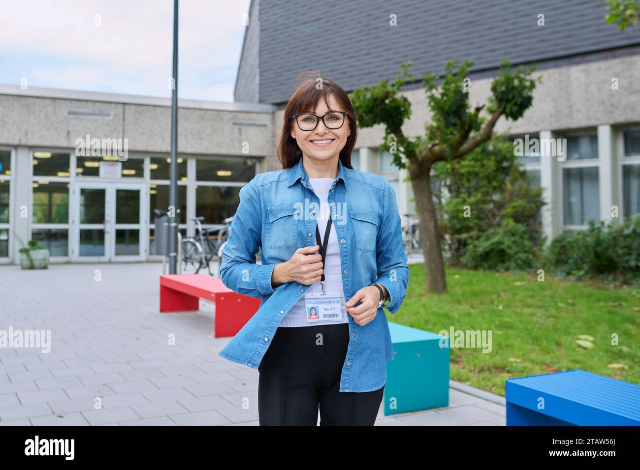 Lehrerin mittleren Alters posiert vor dem Hintergrund des Schulgebäudes Stockfoto