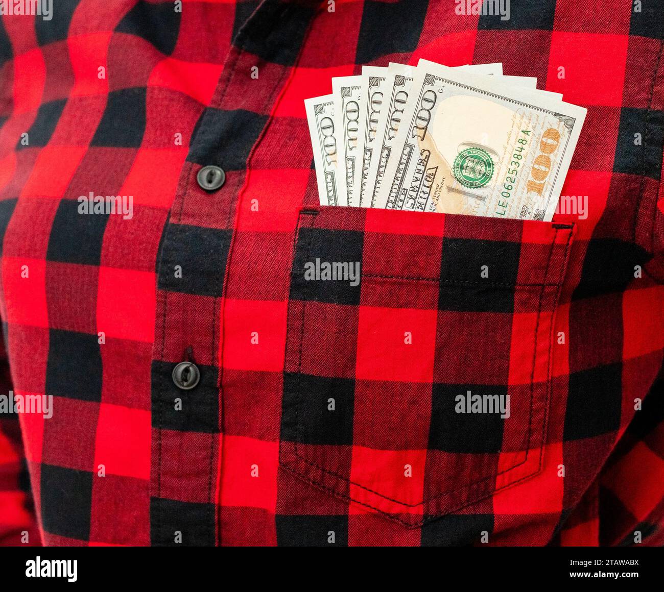 100 Dollar Scheine in einer Tasche mit rotem Hemd aus der Nähe. Weibliche Person und Bargeld in der Brusttasche. Stockfoto